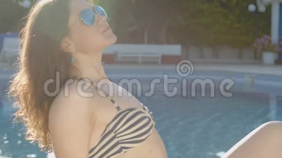 年轻漂亮的女人躺在游泳池附近放松暑假假期视频的预览图