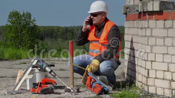 建筑工人在靠近未完工建筑的智能手机上交谈视频的预览图