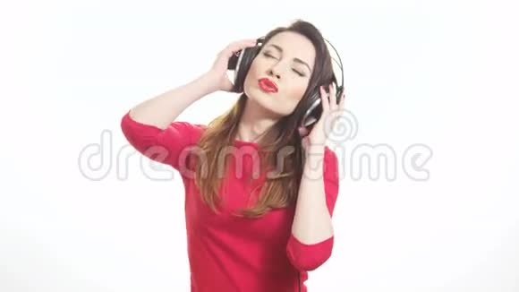 戴着红色口红的漂亮女人听着音乐触摸大耳机摘下耳杯说着什么被隔离在白色上视频的预览图