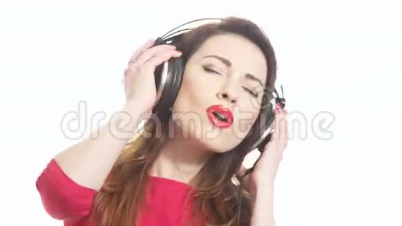 戴着红色口红的漂亮女人听着音乐触摸大耳机摘下耳杯说着什么被隔离在白色上视频的预览图