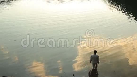 年轻的乡下人站在美丽的湖里在清澈的蓝色水中反射多云的日落天空夏日阳光明媚视频的预览图