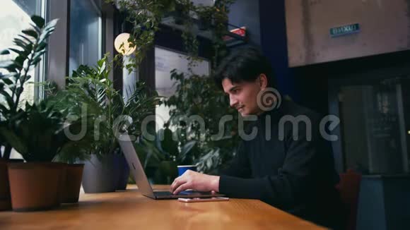 混合种族男子在咖啡馆里用笔记本电脑和智能手机工作视频的预览图