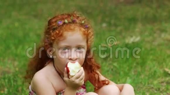 小女孩在绿色夏日公园的草坪上吃苹果视频的预览图
