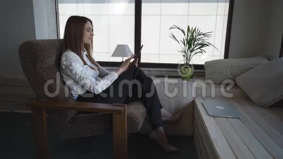 快乐的女商人坐在扶手椅上拿着平板电脑休息一下视频的预览图