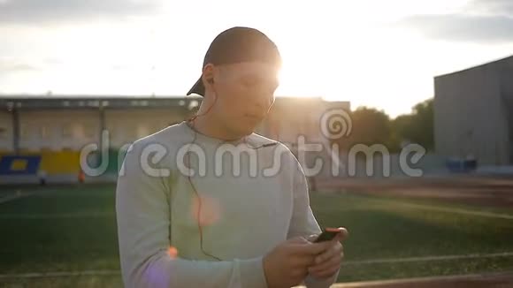 运动缓慢的年轻人戴着耳机在球场跑道上的日落视频的预览图