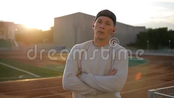 运动缓慢的年轻人戴着耳机在球场跑道上的日落视频的预览图