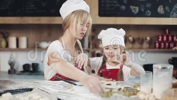 妈妈和女儿穿着同样的衣服在舒适的厨房里准备面团玩得很开心烹饪妈妈和女儿的概念视频的预览图