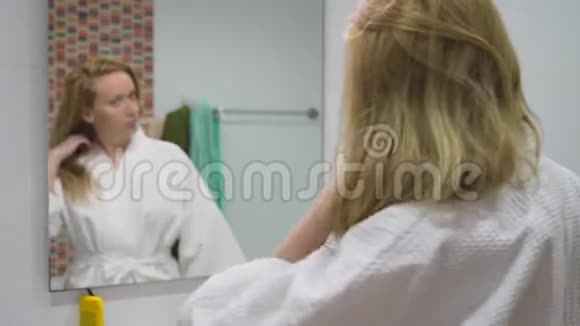 发健康脱发理念女人在浴室里梳着她那金发受损的干头发视频的预览图