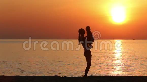日出时妈妈和孩子在沙滩上玩耍的剪影视频的预览图