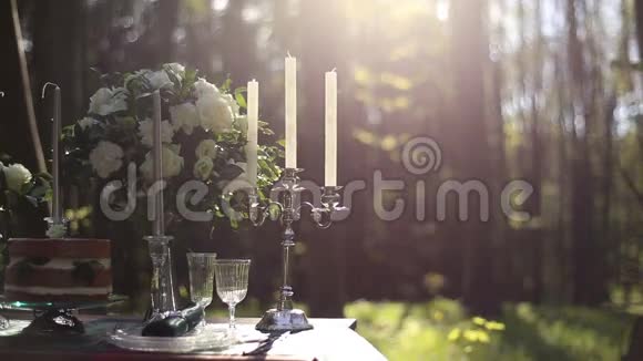 在森林里的婚礼装饰的桌子上合上白色老式烛台背景上的白色玫瑰花束视频的预览图