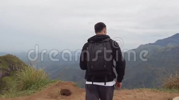 男性徒步旅行者到达山顶伸出手臂向上带背包的年轻人站在边上视频的预览图