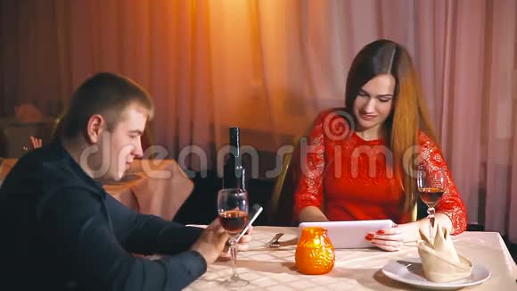 男人和女孩在咖啡馆里带着智能手机和平板电脑晚上爱浪漫的情人节视频的预览图