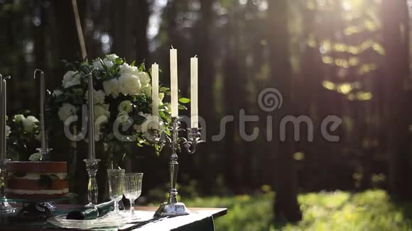 由白色老式烛台和白色玫瑰花束组成的婚礼装饰在森林的桌子上浪漫浪漫视频的预览图