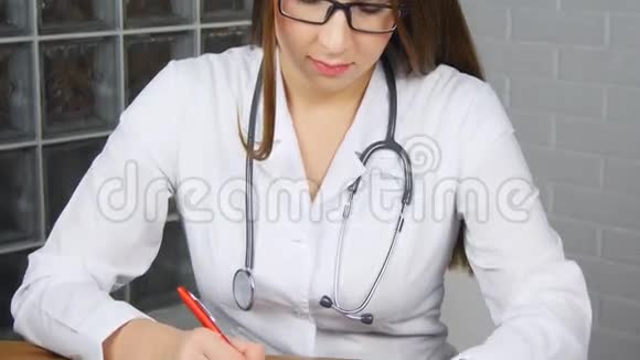 美丽的年轻女医生坐在工作桌前端着一罐药片开着处方视频的预览图
