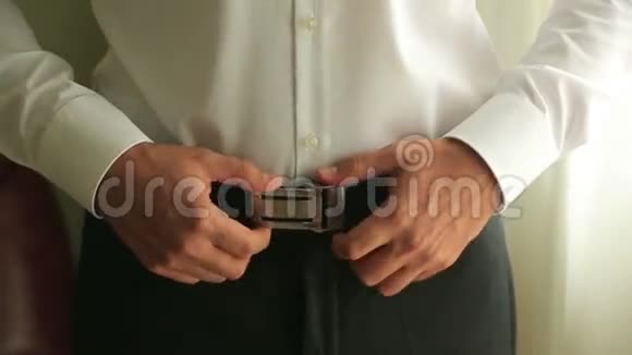 一个新郎的特写调整他裤子上的腰带为婚礼做准备视频的预览图