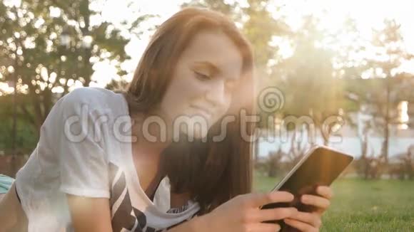 有平板电脑的女人在草地上看视频视频的预览图