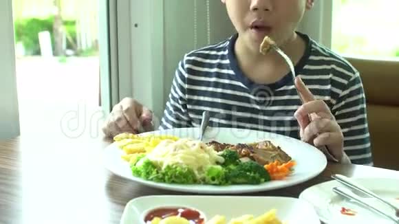 小亚洲男孩在餐厅吃牛排和蔬菜沙拉微笑着面对视频的预览图