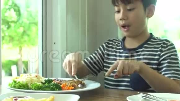 小亚洲男孩在餐厅吃牛排和蔬菜沙拉微笑着面对视频的预览图