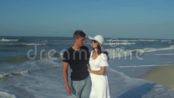 年轻漂亮的夫妇走在海边男孩和女孩他们很开心阳光灿烂慢动作海浪视频的预览图