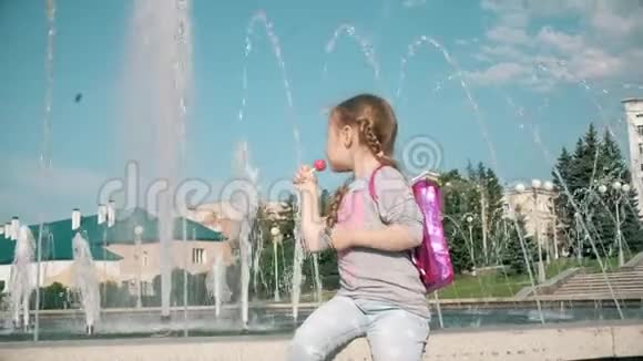 在阳光明媚的一天美丽的女孩在喷泉附近吃棒棒糖视频的预览图