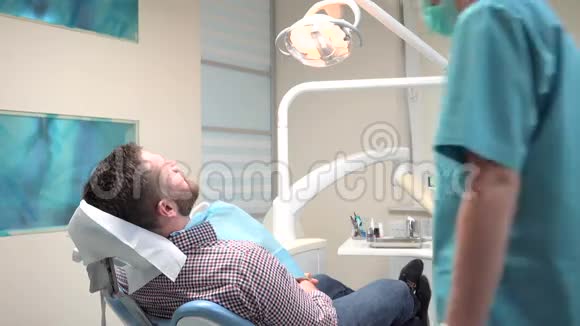 女牙医坐下来检查男性病人的牙齿视频的预览图