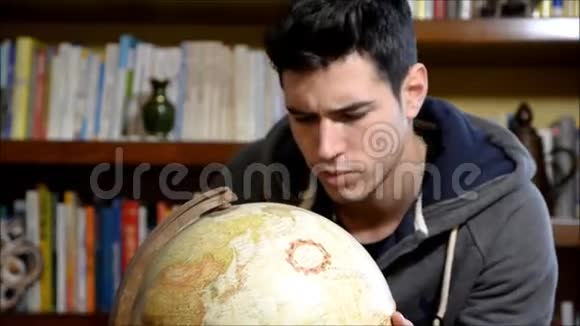 英俊的年轻人拿着一个地球仪在家里看着摄像机视频的预览图