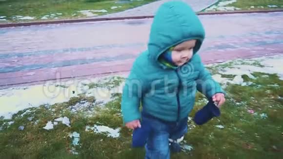 春天斯塔迪加姆的一个孩子从人行道上跑下来草地和融化的雪慢动作视频的预览图