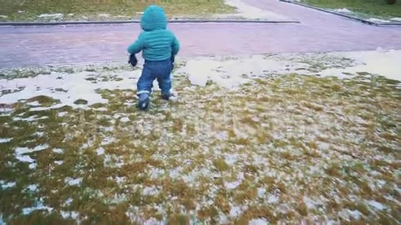 春天斯塔迪加姆的一个孩子从人行道上跑下来草地和融化的雪慢动作视频的预览图