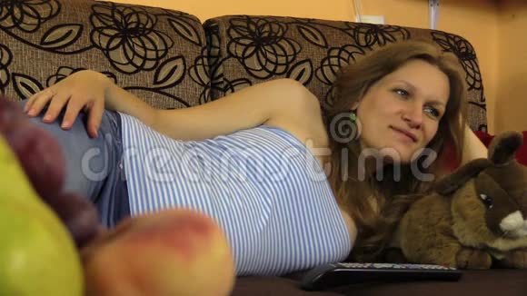 女孩在沙发上看电视手里拿着遥控器玩具兔子水果视频的预览图