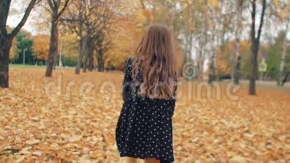 快乐可爱的卷发小女孩穿着圆点花纹的裙子穿过公园里的秋巷视频的预览图