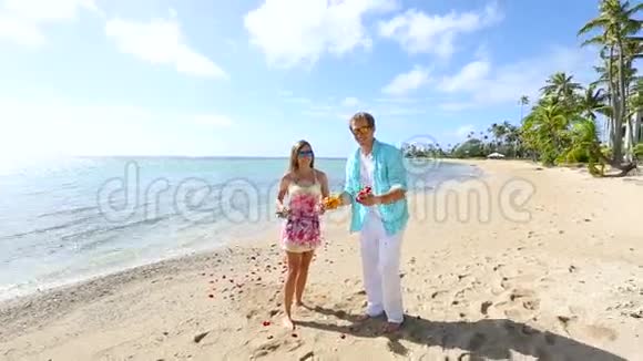 快乐的年轻夫妇在海滩上玩着许多玫瑰花瓣视频的预览图