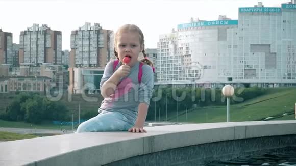 在阳光明媚的一天美丽的女孩在喷泉附近吃棒棒糖视频的预览图