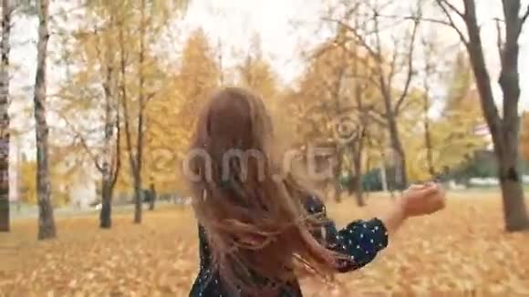 快乐可爱的卷发小女孩穿着圆点花纹的裙子穿过公园里的秋巷视频的预览图