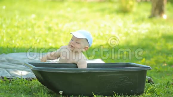 小男孩坐在绿色花园的盆地附近美丽的宝宝微笑着打着水涨船高视频的预览图