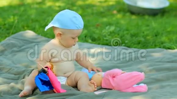 可爱的小男孩带着一个小娃娃和婴儿车在花园里视频的预览图