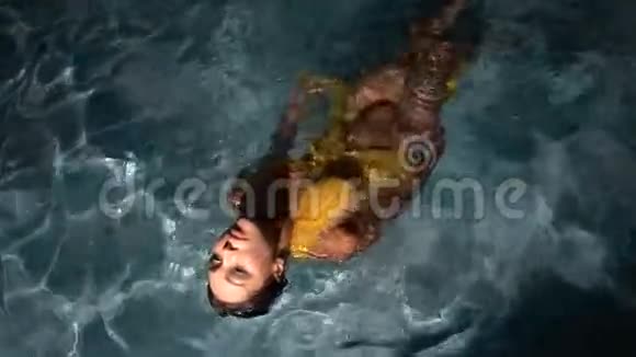 在游泳池里穿着黄色连衣裙的美丽黑发女人视频的预览图