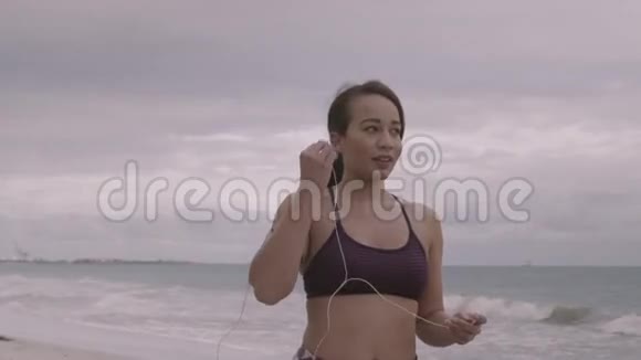 在阴天准备在海滩上慢跑的年轻女子健身慢动作视频的预览图