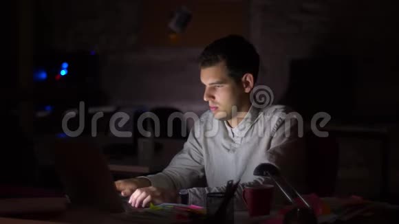拍摄黑暗的办公室屏幕上的光线照射在他的脸上而他正在坐着看电脑和检查视频的预览图