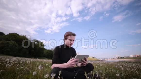 年轻人带着平板电脑坐在公园里聊天冲浪学习视频的预览图