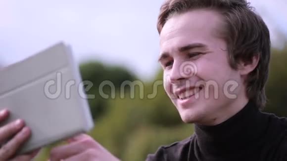 年轻人带着平板电脑坐在公园里聊天冲浪学习看上去很开心视频的预览图