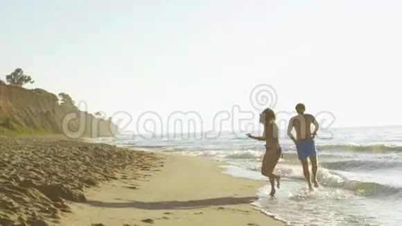 快乐的年轻夫妇在海边玩海浪在沙滩上慢动作视频的预览图