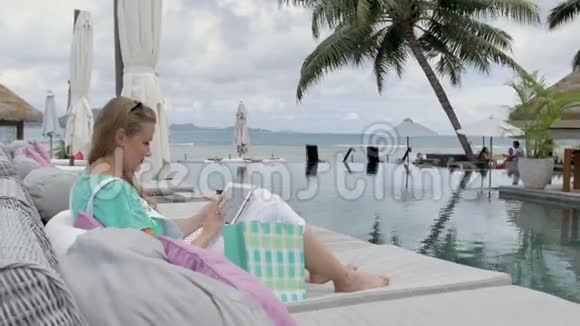在度假期间带着太阳镜的开朗女人坐在酒店休息室里使用数字平板电脑视频的预览图