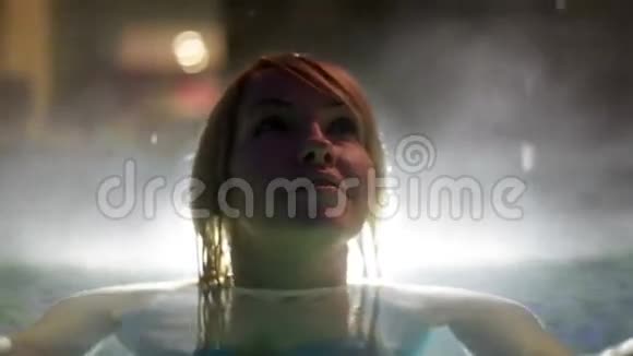 穿着蓝色比基尼的年轻女子晚上在室外游泳池里捕捉雪花视频的预览图