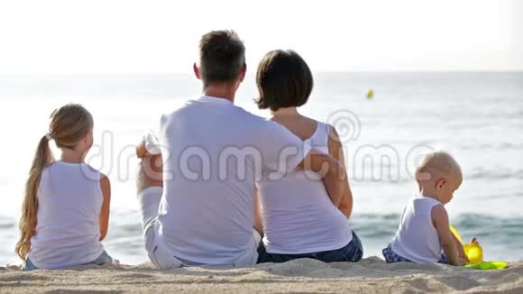一男一女带着两个孩子坐在沙滩上对着镜头视频的预览图