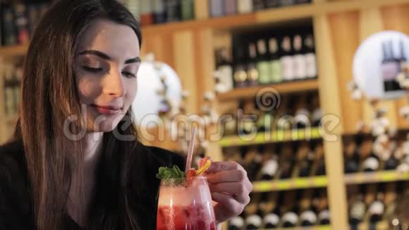 一个年轻的女孩在时尚餐厅的桌子上喝一杯鸡尾酒女人喝红色的异国鸡尾酒视频的预览图