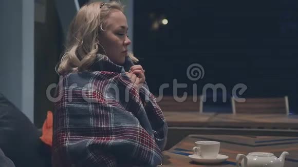 一个年轻漂亮的金发女人到街头咖啡馆的形象金发女郎用温暖的毯子喝茶听着视频的预览图