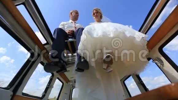 年轻快乐的新婚夫妇在复古巴士顶部的田野下面的视图视频的预览图