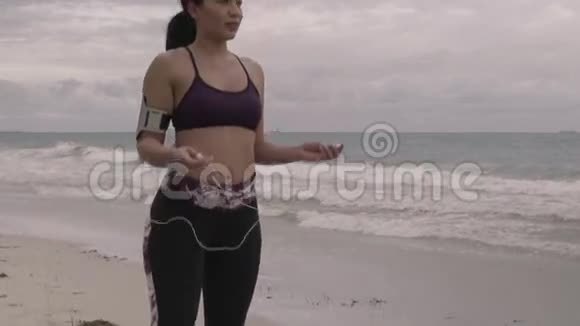 在阴天准备在海滩上慢跑的年轻女子健身慢动作视频的预览图