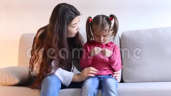 年轻的母亲和小女儿坐在客厅的沙发上视频的预览图