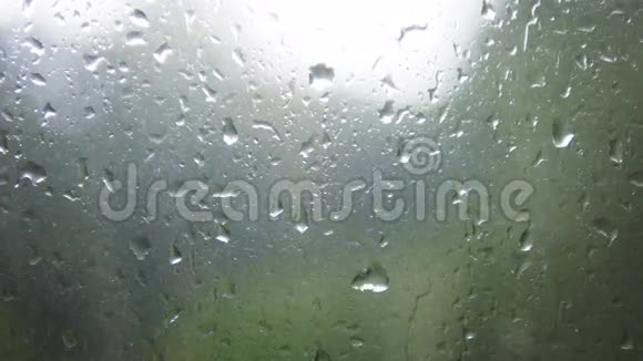 玻璃上水滴的特写雨滴在模糊背景的窗户玻璃上模糊的树和天空雨天视频的预览图